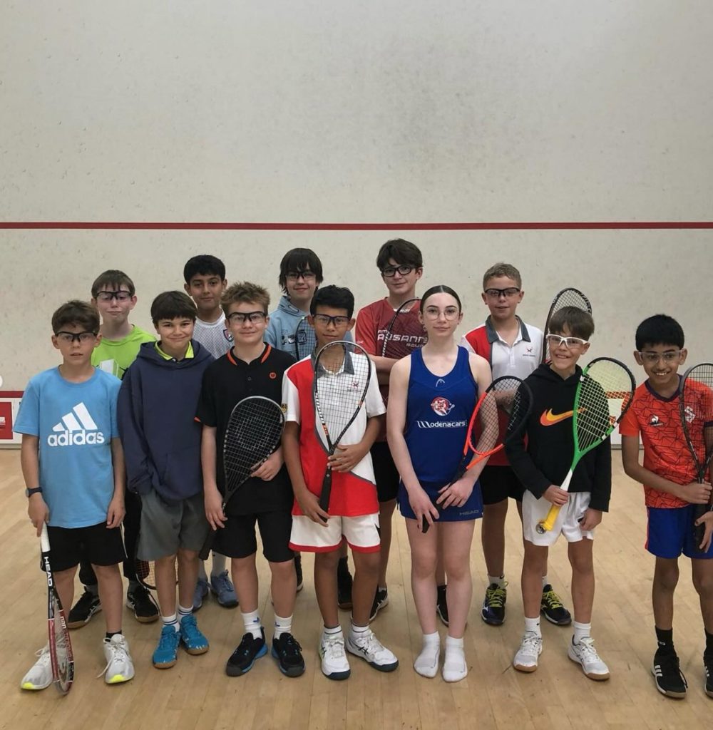 Une douzaine de juniors, lunettes de protection et raquettes en main, posent sur un court aux Championnats romands 2024
