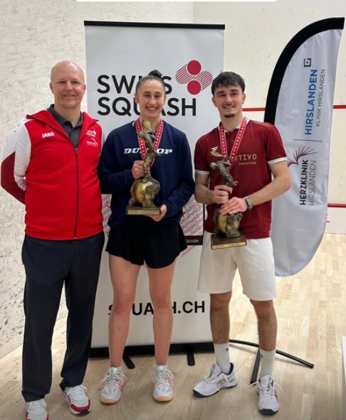 Ambre Allinckx et David Bernet, champions suisses 2026, posent avec leur trophée devant un panneau Swiss Squash, aux côtés d'un membre de l'encadrement