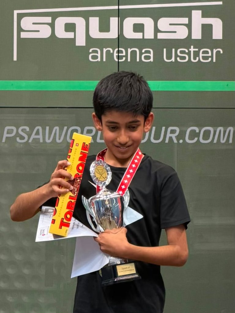 Un jeune joueur brandit sa coupe, sa médaille et son prix devant le mur de la Squash Arena Uster