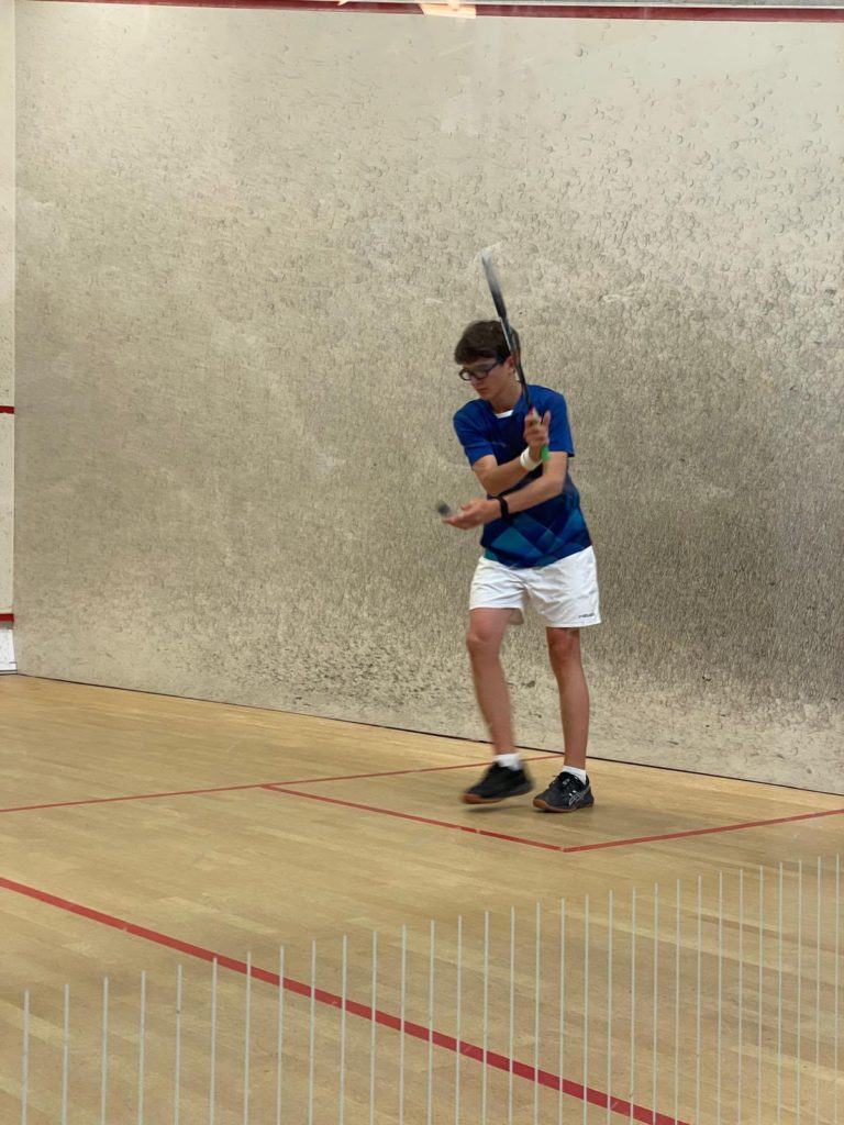 Un junior en maillot bleu frappe la balle en revers