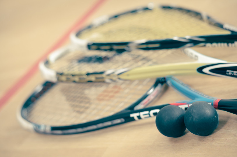 Trois raquettes et deux balles de squash posées sur le parquet d'un court